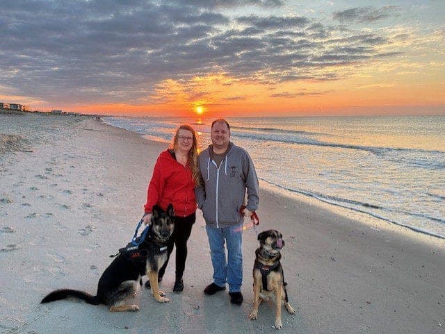Michelle and Carson on the beach at sunset with their dogs, Jax and Tallulah